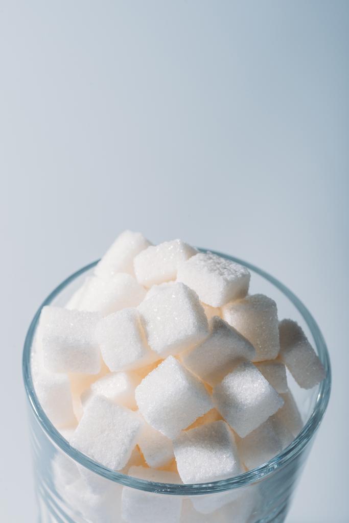 білі солодкі цукрові кубики в склянці на сірому фоні
  - Фото, зображення
