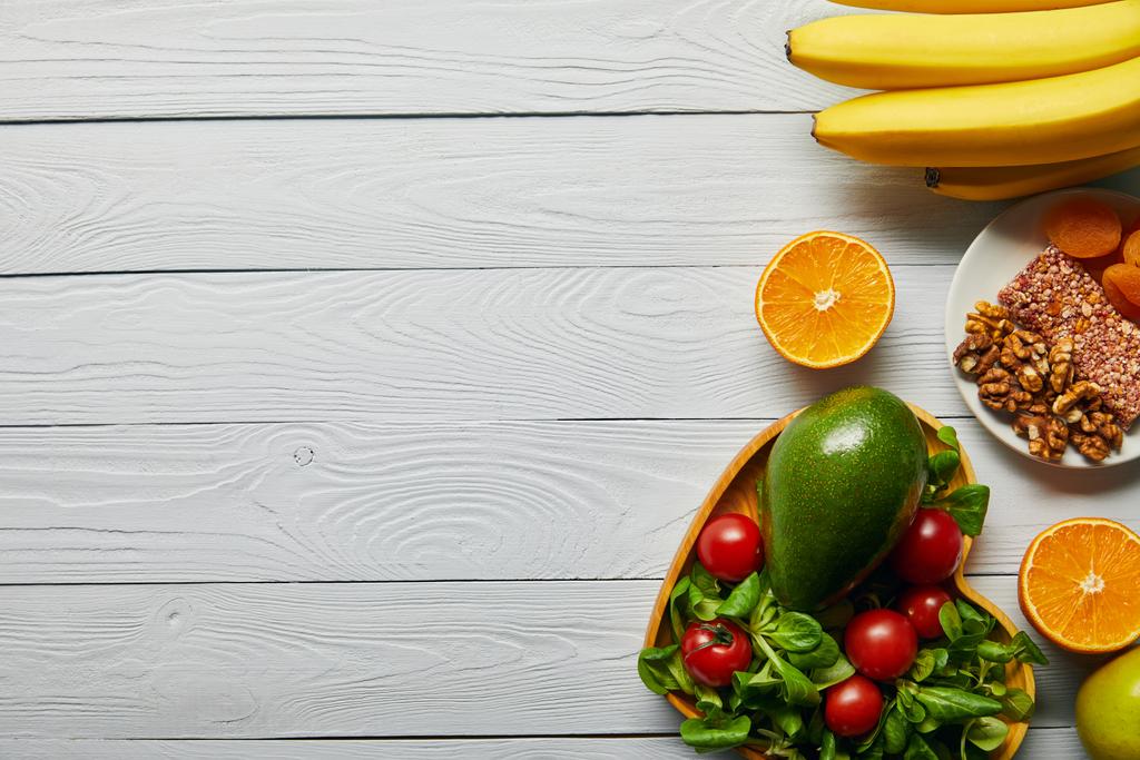 Draufsicht auf frisches Obst, Gemüse in herzförmiger Schüssel auf hölzernem weißem Hintergrund mit Kopierraum - Foto, Bild