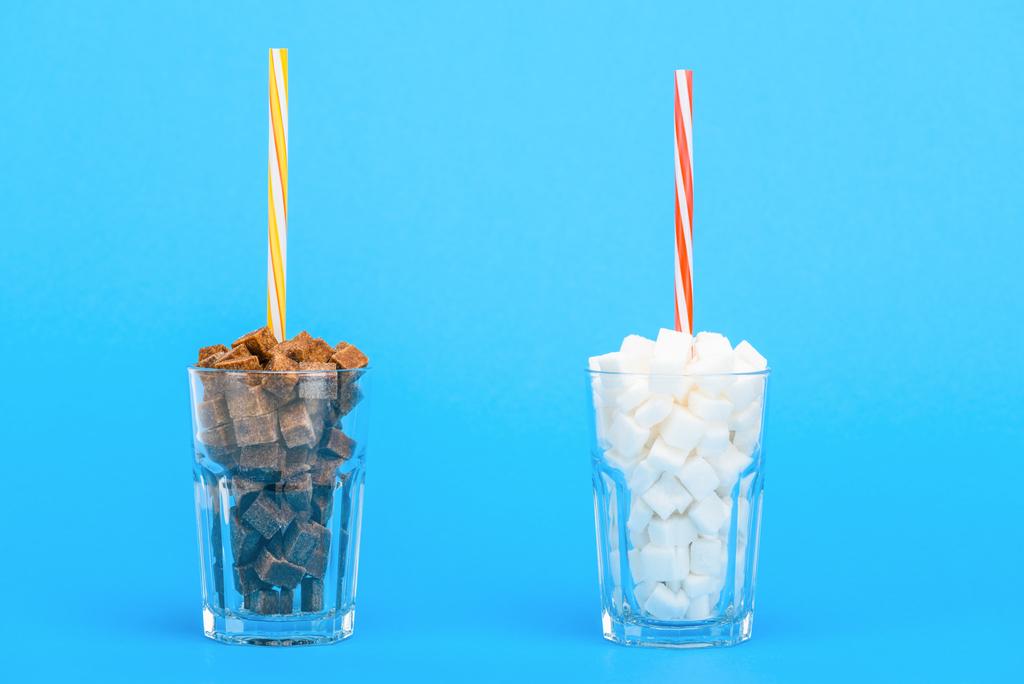 Gläser mit Strohhalmen und weißen und braunen Zuckerwürfeln auf blauem Hintergrund - Foto, Bild