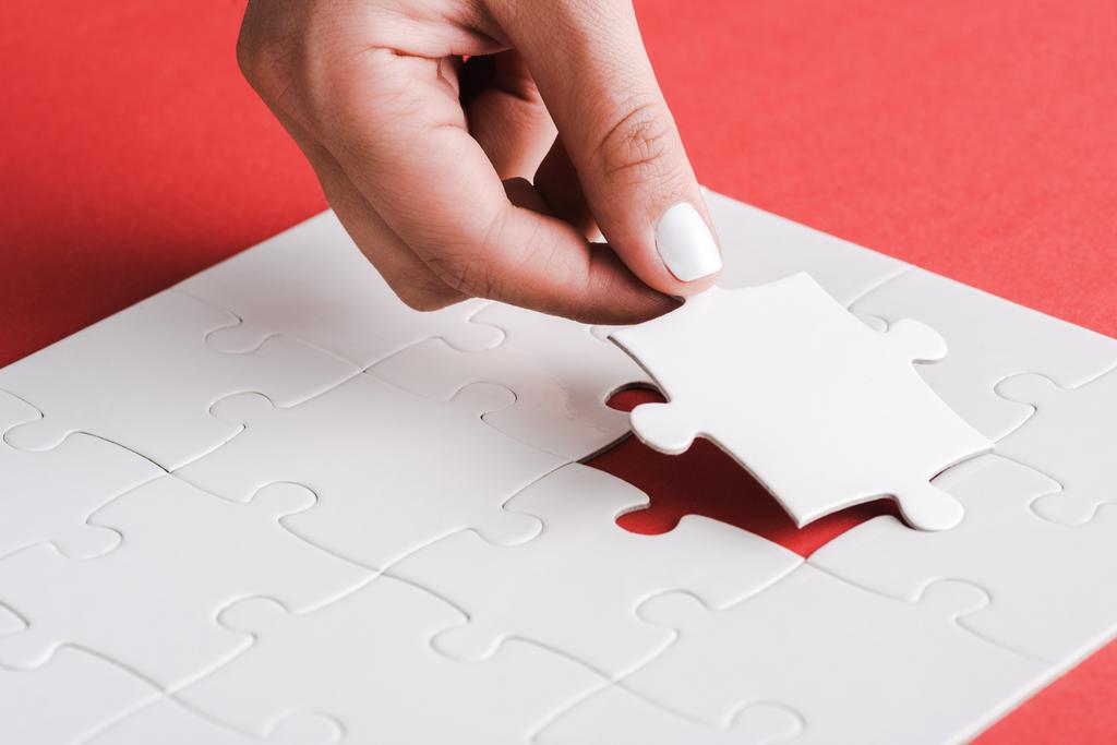 vista ritagliata di donna che tiene puzzle bianco vicino a pezzi di puzzle collegati sul rosso
 - Foto, immagini