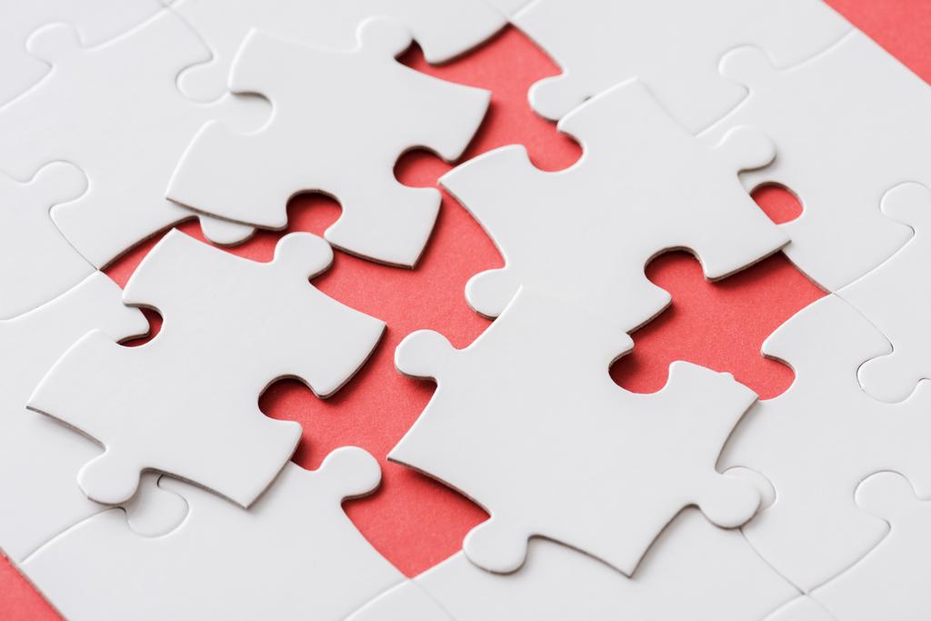 unfertige Puzzleteile in der Nähe miteinander verbundener weißer Puzzleteile auf rot  - Foto, Bild