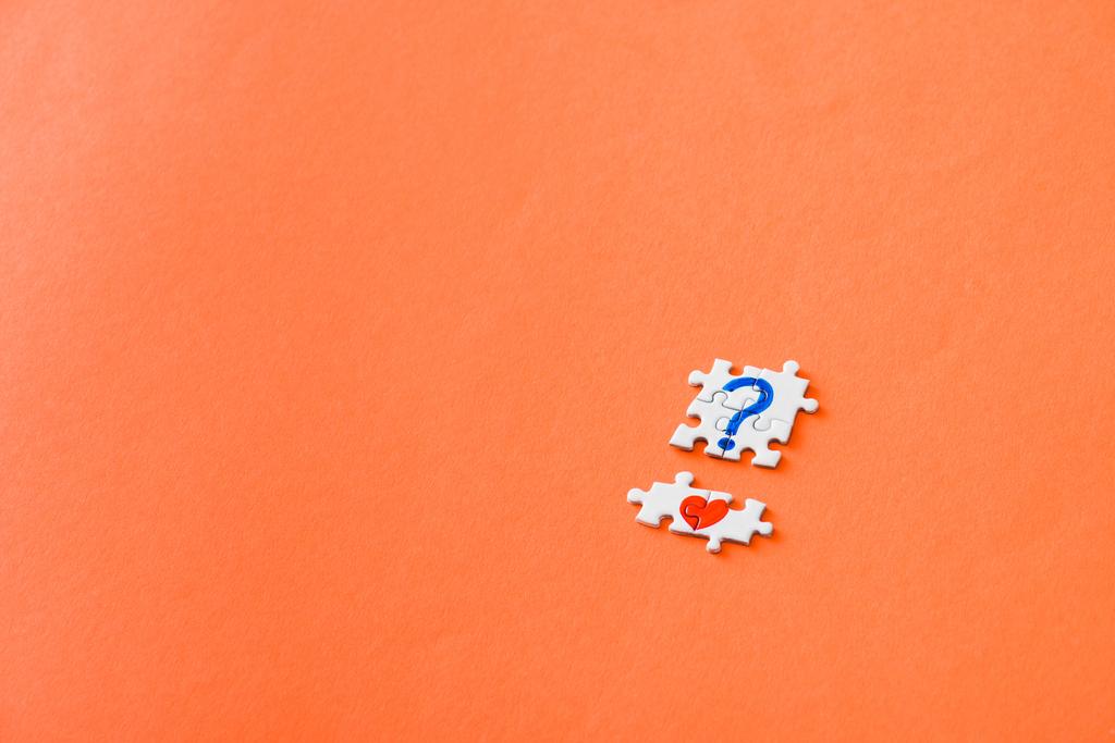 vue du haut de petites pièces de puzzle connectées avec coeur rouge dessiné et point d'interrogation bleu sur orange
 - Photo, image