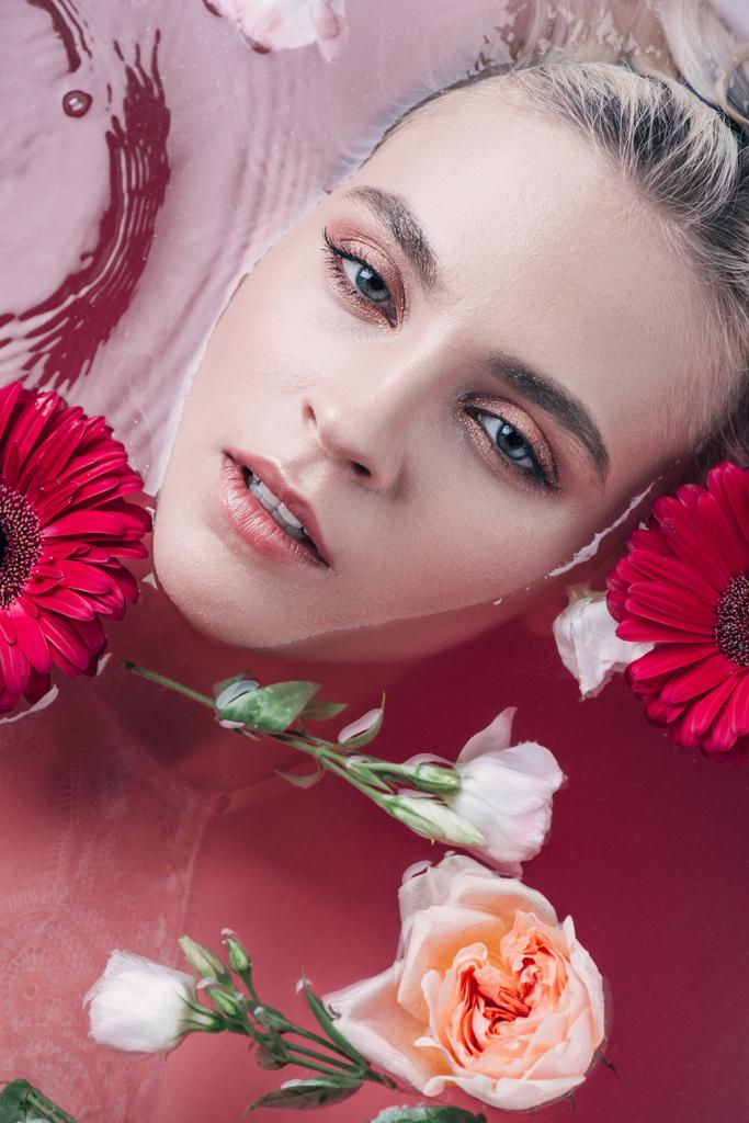 Draufsicht der schönen jungen Frau in der Badewanne liegend mit farbigem rosa Wasser und Blumen - Foto, Bild