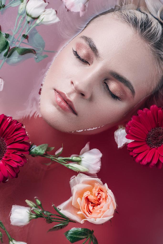 вид зверху красива молода жінка з закритими очима лежить у ванні з кольоровою рожевою водою і квітами
 - Фото, зображення