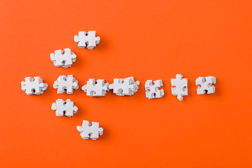 bovenaanzicht van witte richtingspijl met puzzelstukjes op oranje - Foto, afbeelding