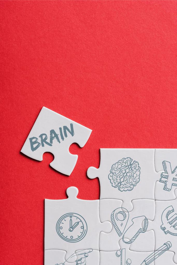 Draufsicht auf unfertige weiße Puzzles in der Nähe separaten Teils mit Gehirn Schriftzug isoliert auf rot  - Foto, Bild