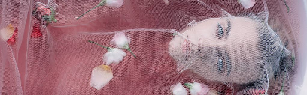 vista dall'alto di bella donna ricoperta di tessuto a rete bianca in acqua rosa con petali di rosa, colpo panoramico
 - Foto, immagini