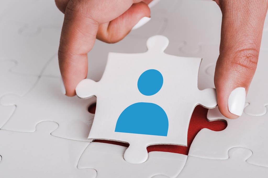 Nahaufnahme einer Frau, die ein weißes Puzzle mit blauem menschlichen Symbol in der Nähe miteinander verbundener Puzzleteile hält - Foto, Bild
