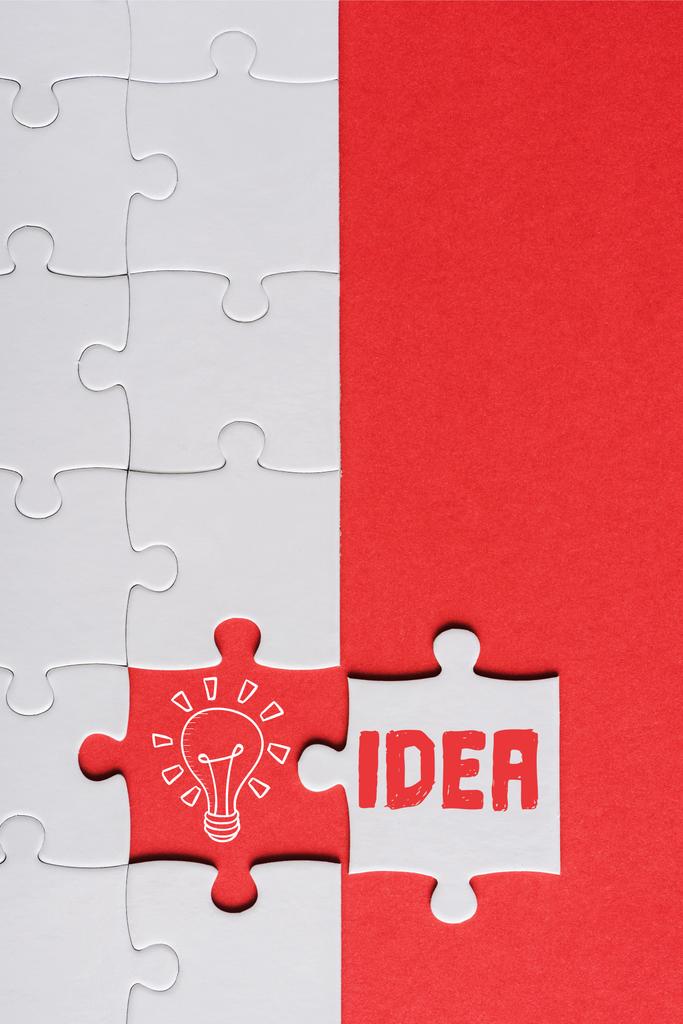 top view of incomplete jigsaw near white puzzle piece with idea lettering isolated on red - Photo, Image