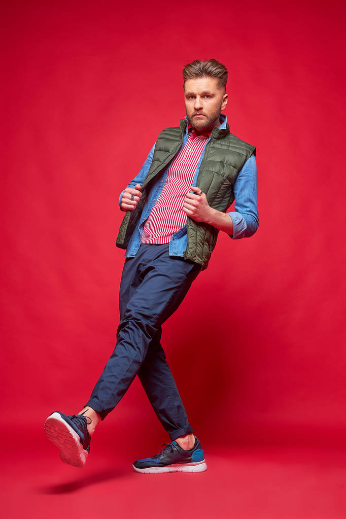 Mužský model pózný v příležitostných šatech. Módní portrét, snímek studia, červené pozadí - Fotografie, Obrázek