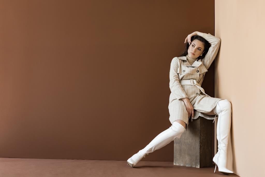 μοντέρνα γυναίκα σε καμπαρντίνα και λευκές μπότες σε καφέ φόντο με χώρο αντιγραφής - Φωτογραφία, εικόνα