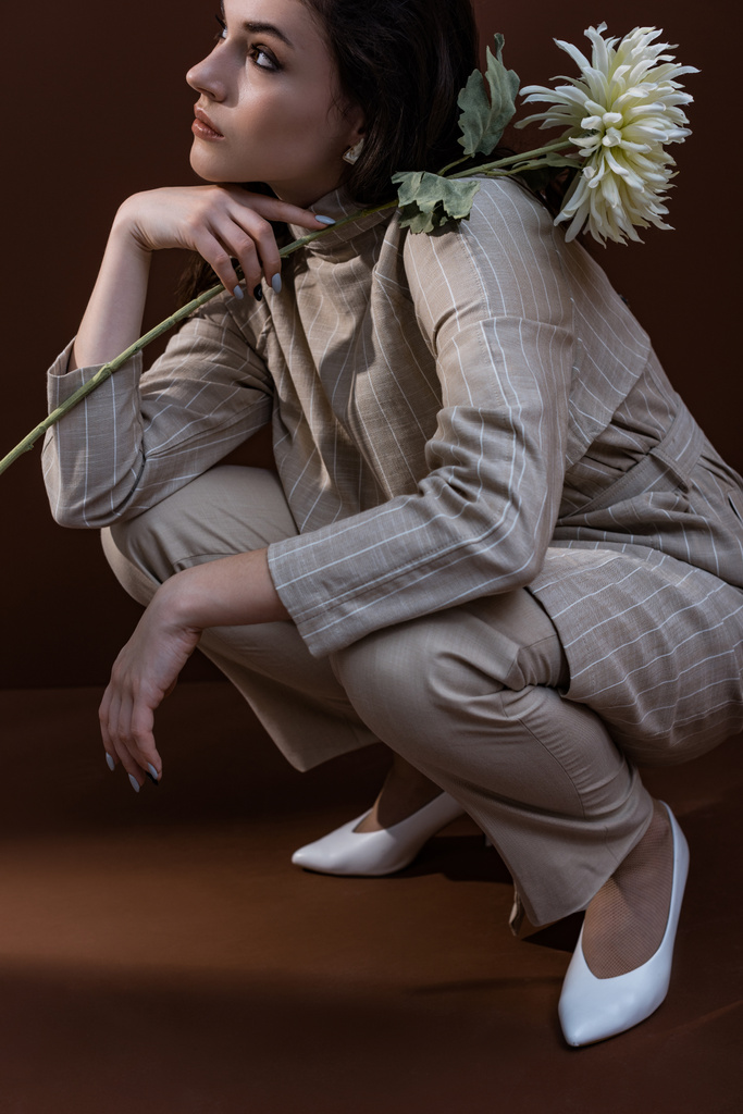 donna adulta con crisantemo bianco in mano, seduta su sfondo marrone
 - Foto, immagini