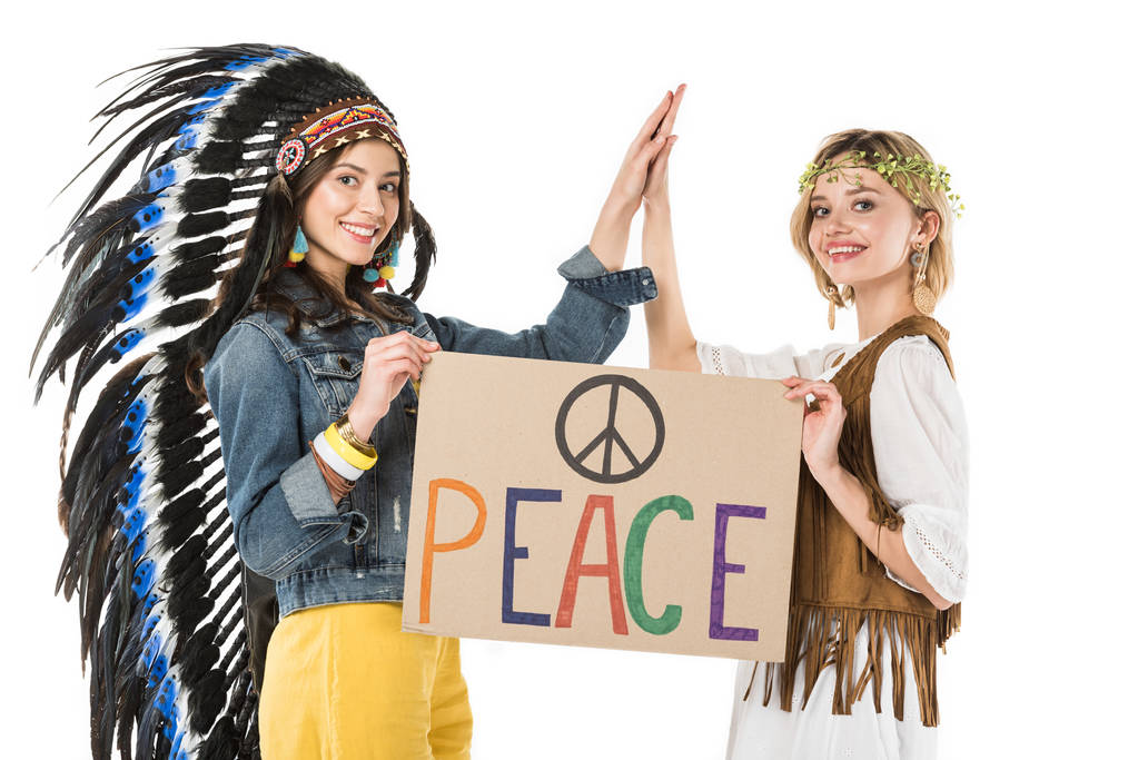 dos chicas hippies bisexuales sonrientes en tocado indio y guirnalda sosteniendo pancarta con inscripción y tocando manos aisladas en blanco
 - Foto, imagen