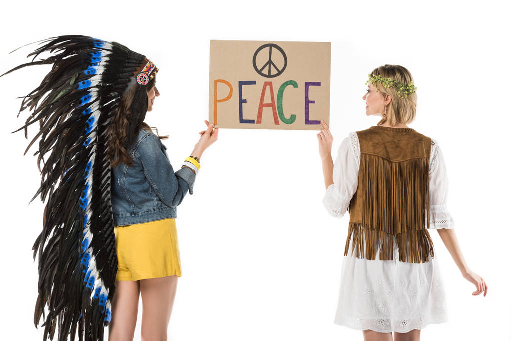 Rückansicht zweier bisexueller Hippie-Mädchen in indischer Kopfbedeckung und Kranz mit Plakat mit Inschrift isoliert auf weißem Grund - Foto, Bild