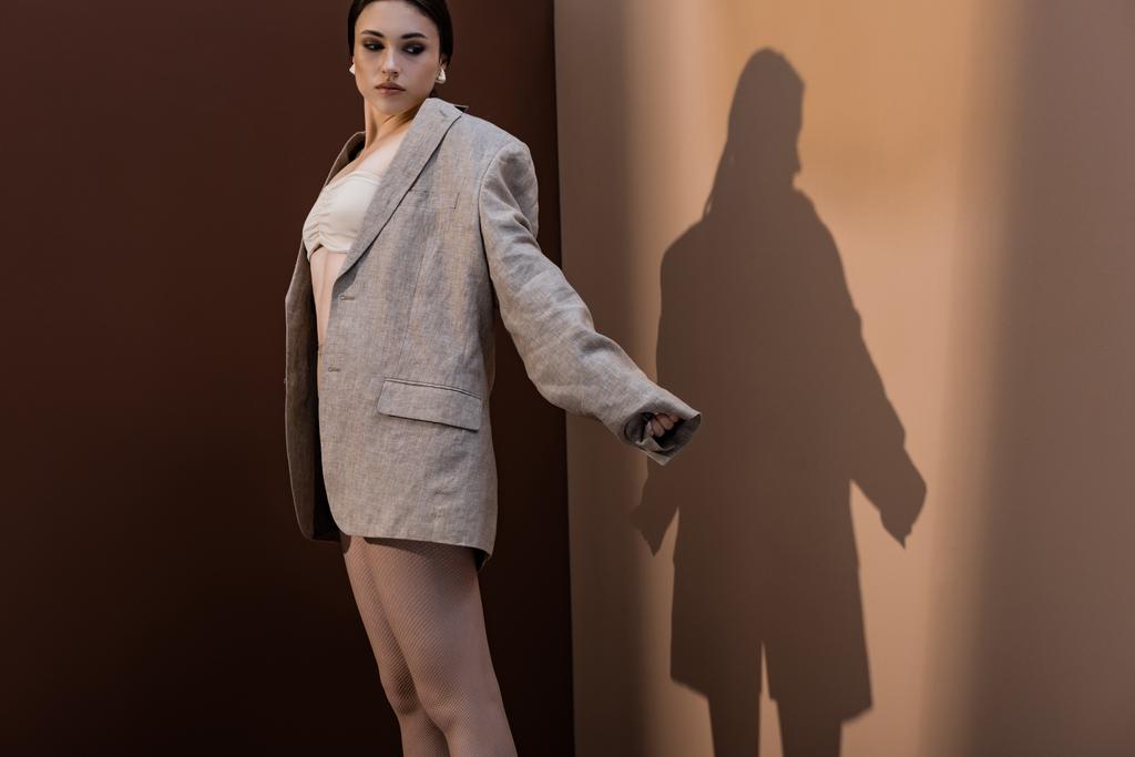 mujer de moda en ropa interior y chaqueta de pie sobre fondo marrón, mirando hacia otro lado
 - Foto, Imagen