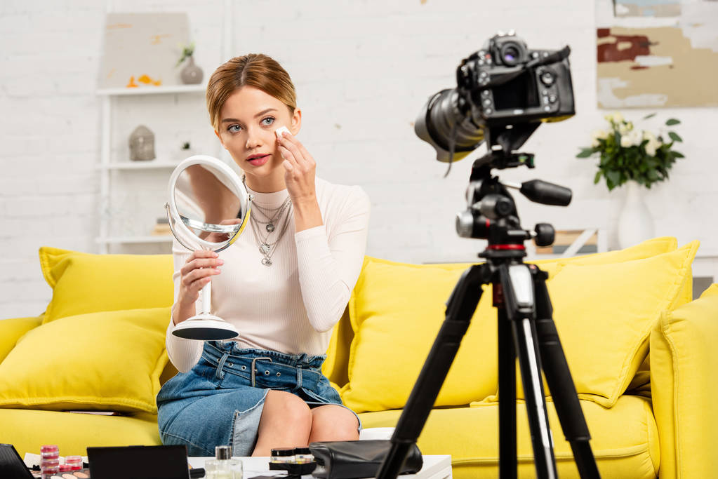 blogger de belleza sonriente con espejo usando cosméticos decorativos frente a una cámara de video
 - Foto, Imagen