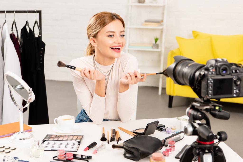 sorridente beauty blogger che tiene pennelli cosmetici davanti alla videocamera
 - Foto, immagini