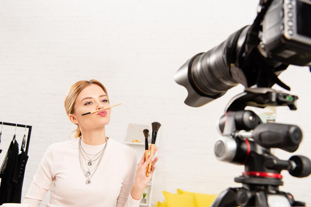 blogger de belleza con cosméticos decorativos sosteniendo pinceles cosméticos delante de la cámara de video
 - Foto, Imagen