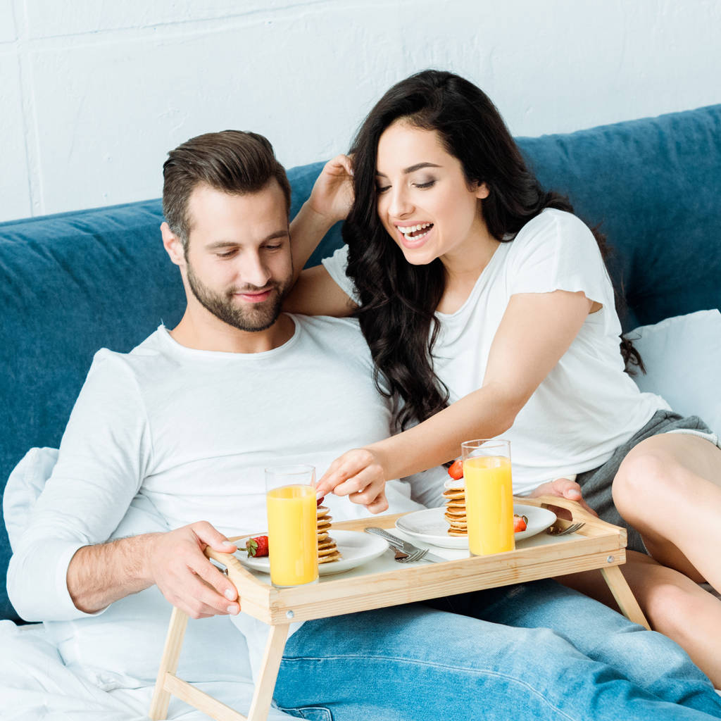 happy couple having orange juice and pancakes for breakfast in bed - Photo, Image