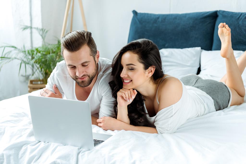 szczęśliwa para patrząc na ekranie laptopa leżąc w łóżku, ilustrujący redakcyjnych - Zdjęcie, obraz