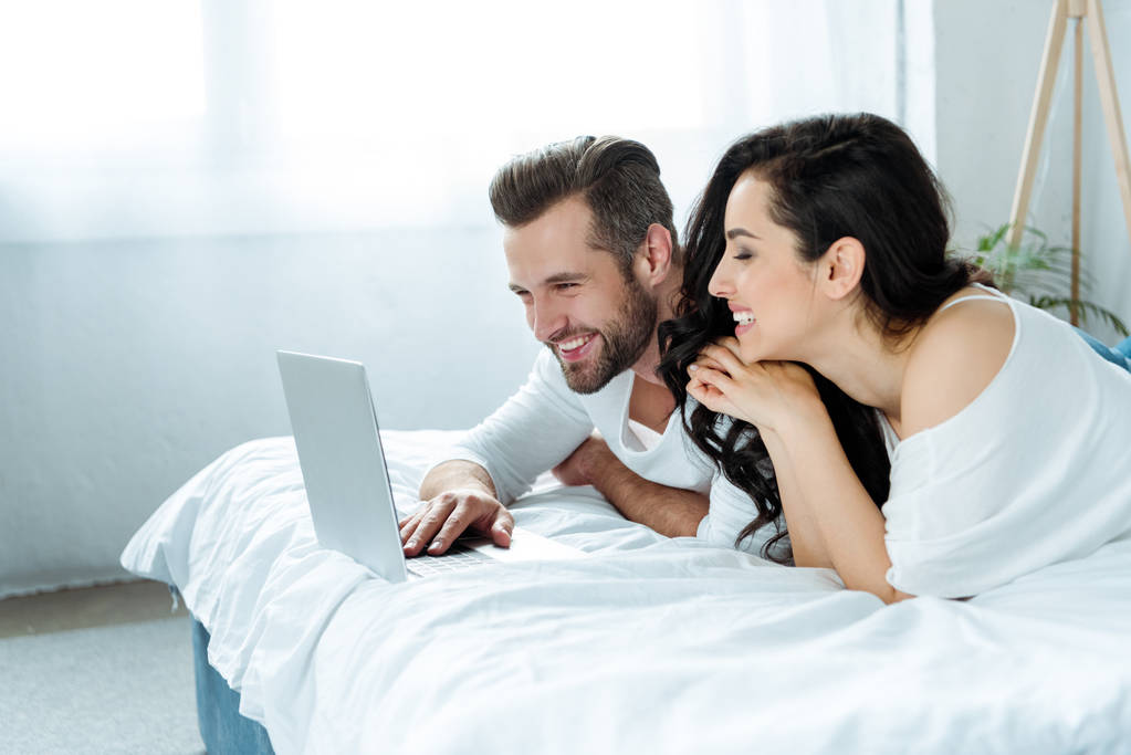 heureux couple souriant en utilisant ordinateur portable au lit ensemble
 - Photo, image