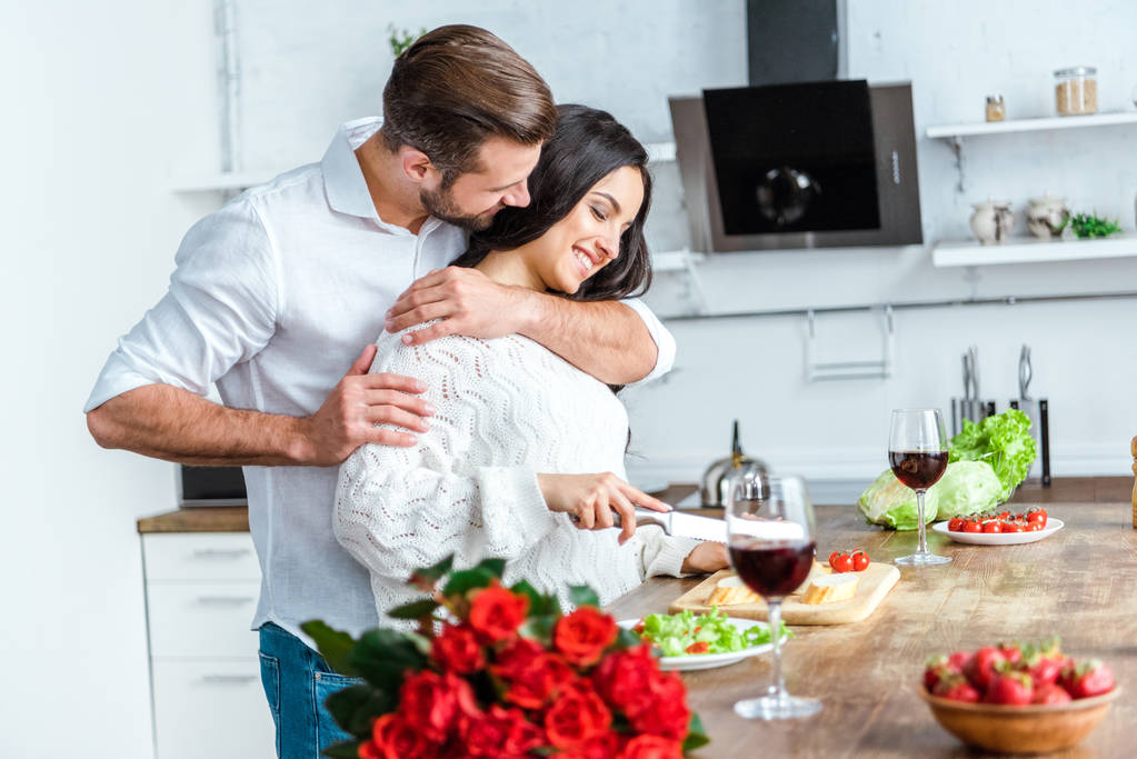 ロマンチックな夕食を調理中に幸せな女性を抱きしめる男 - 写真・画像