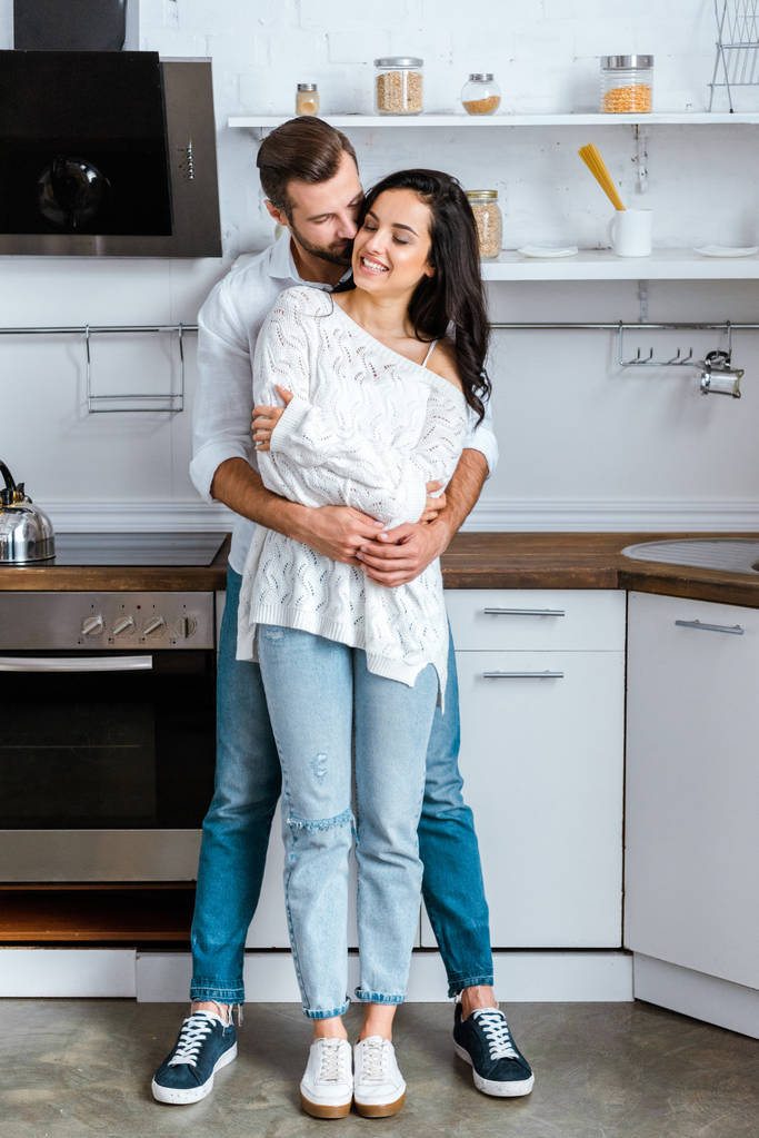 Вид мужчины в полный рост, мягко обнимающего счастливую женщину на кухне
 - Фото, изображение