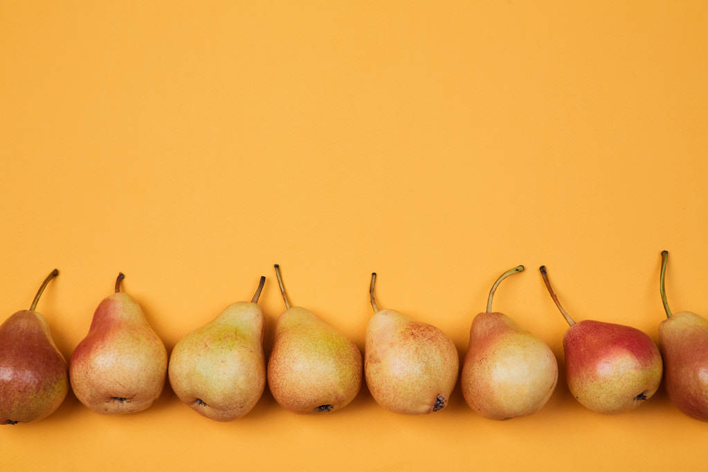Barevný vzorek ovoce nebo pozadí. Složení zralých šťavnatých hrušek umístěných na světle oranžovém pozadí - Fotografie, Obrázek