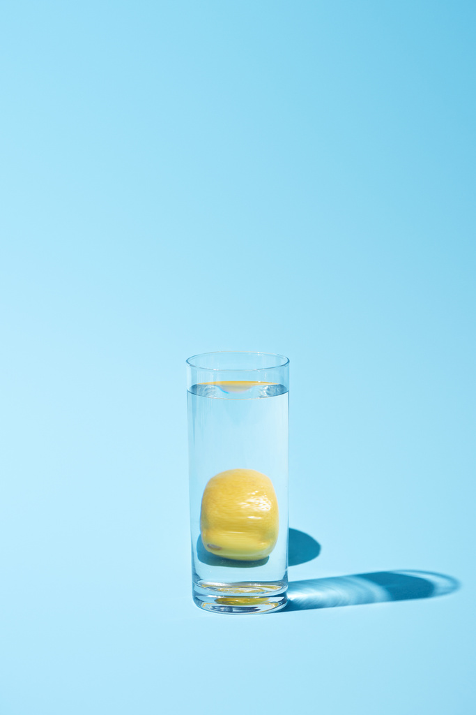 przezroczyste szkło z wodą i całą cytryną na niebieskim tle  - Zdjęcie, obraz