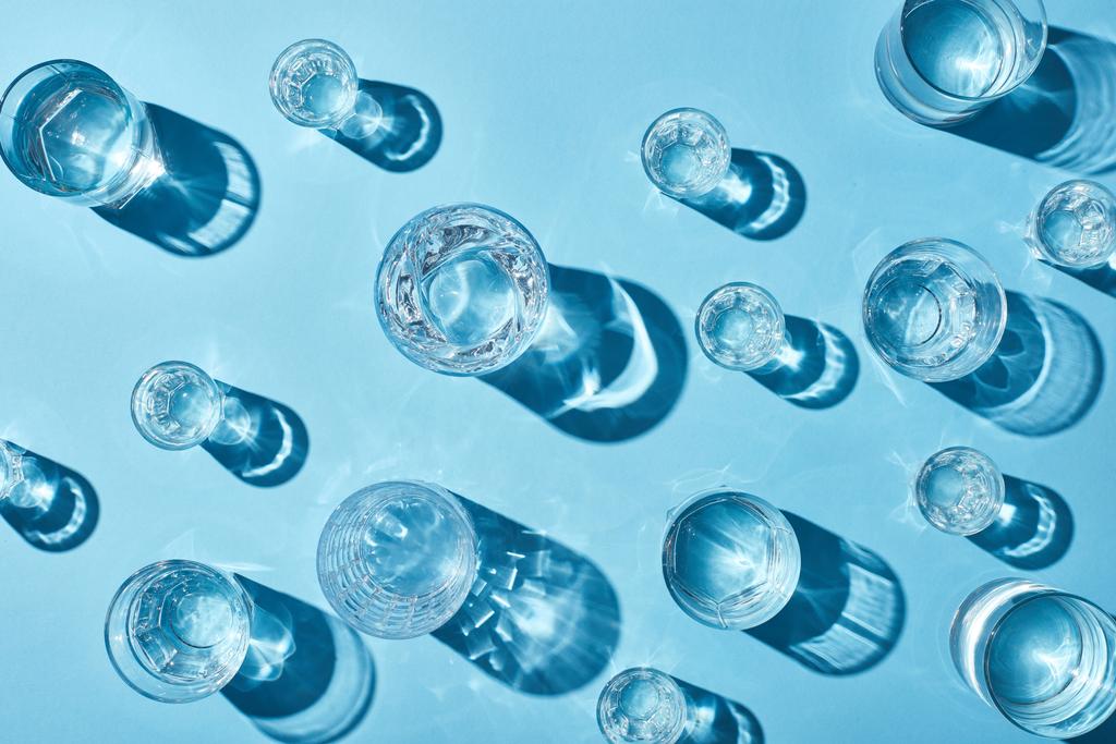 top view of transparent glasses with clear water and shadows on blue background  - Photo, Image