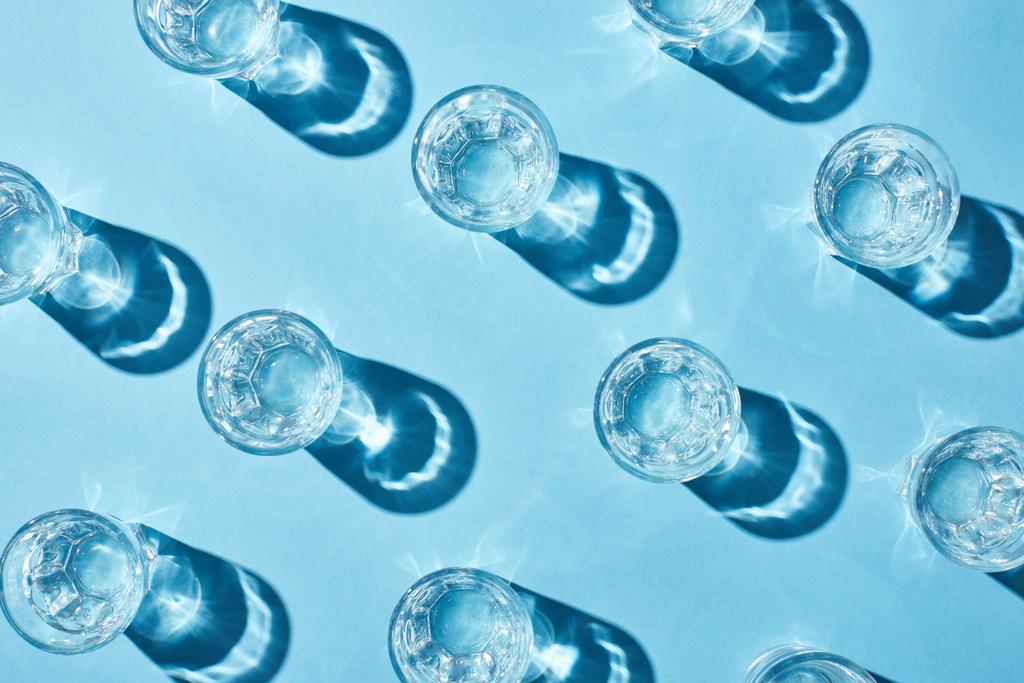 top view of glasses with pure water and shadows on blue surface - Photo, Image