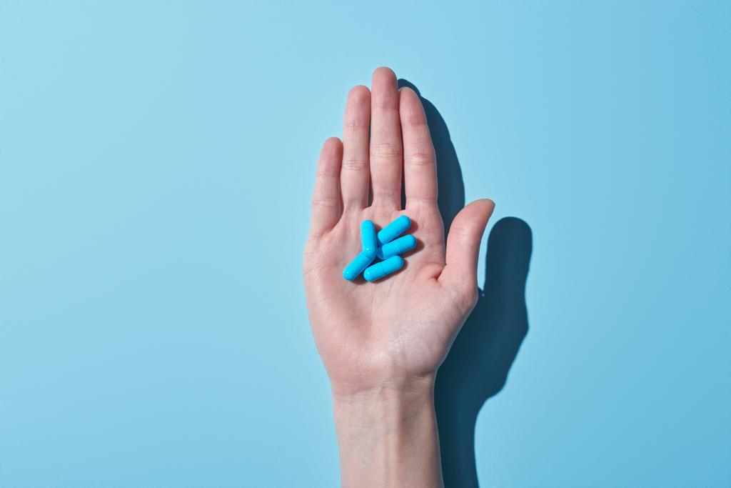 обрезанный вид женщины с голубыми таблетками на ладони на синем фоне
 - Фото, изображение