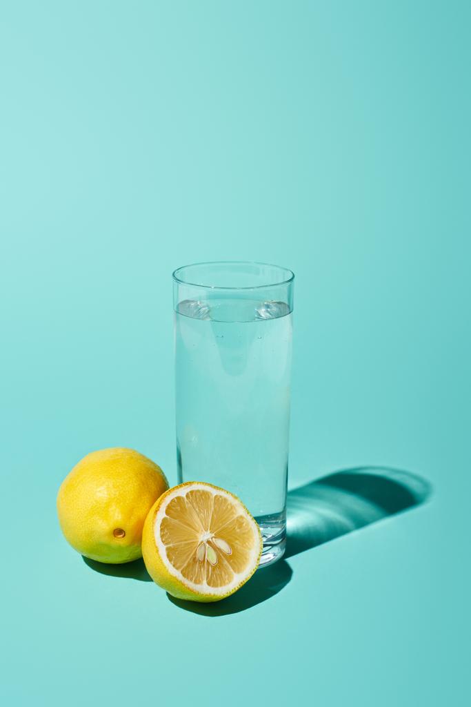 transparent glass with fresh water and bright lemon on turquoise background - Photo, Image