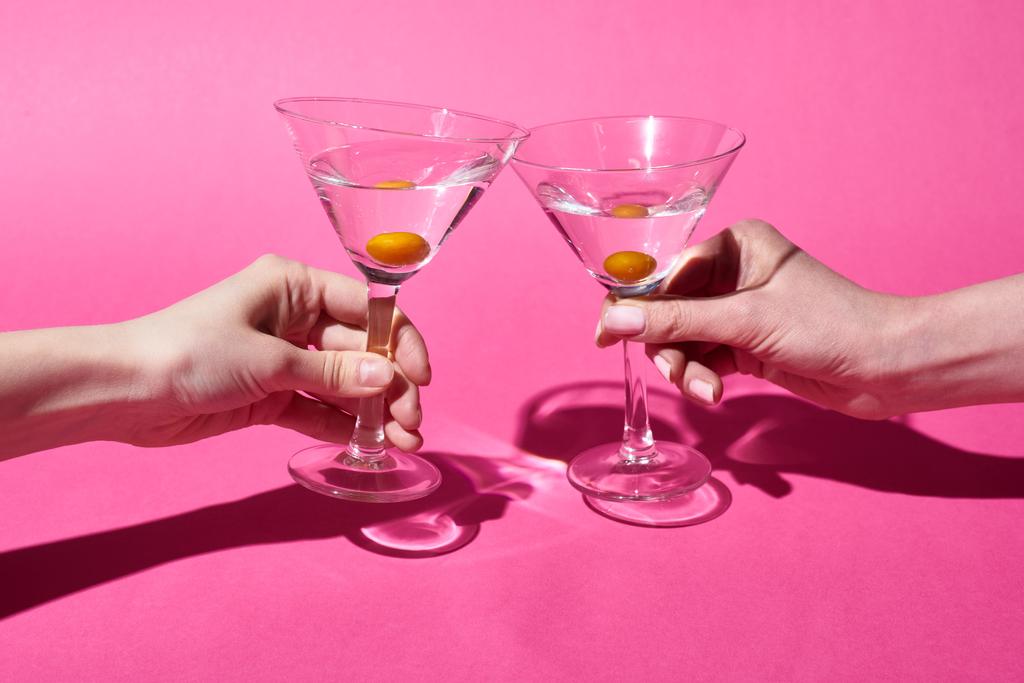 bijgesneden beeld van vrouwen die een bril met cocktails op roze achtergrond houden - Foto, afbeelding