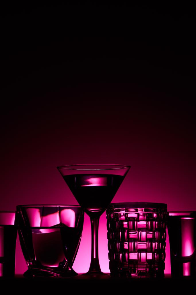 vidros transparentes com líquido no fundo escuro com iluminação rosa
 - Foto, Imagem