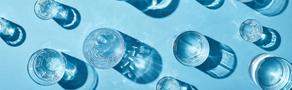 Draufsicht auf transparente Gläser mit klarem Wasser auf blauem Hintergrund, Panoramaaufnahme - Foto, Bild