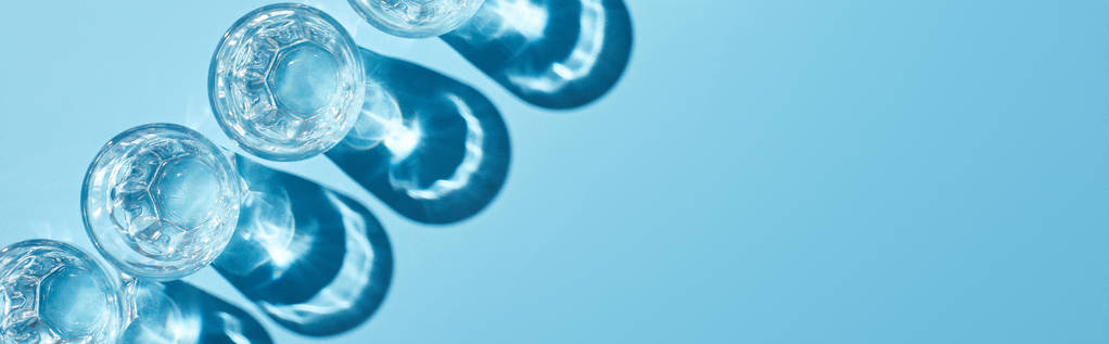 flache Lage mit Gläsern mit klarem Wasser und Schatten auf blauem Hintergrund, Panoramaaufnahme - Foto, Bild