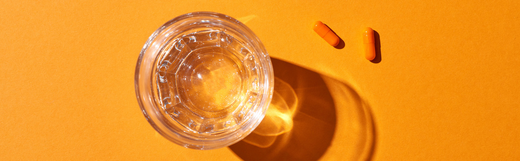 vista superior de las píldoras cerca del vidrio con agua sobre fondo naranja, plano panorámico
 - Foto, imagen