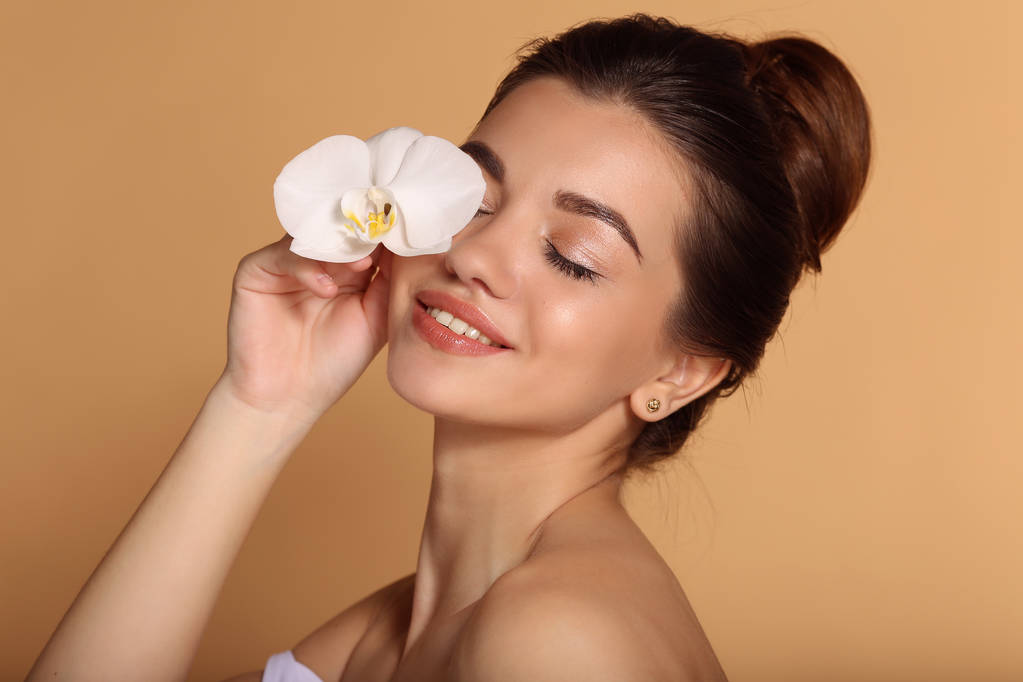 Kusursuz deri ile genç güzel kız Closeup portre elinde beyaz orkide çiçek tutuyor. Cilt bakımı, güzellik ve kozmetik konsepti. - Fotoğraf, Görsel