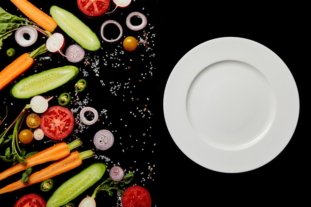 вид зверху порожня кругла тарілка біля овочевих скибочок ізольовано на чорному
 - Фото, зображення