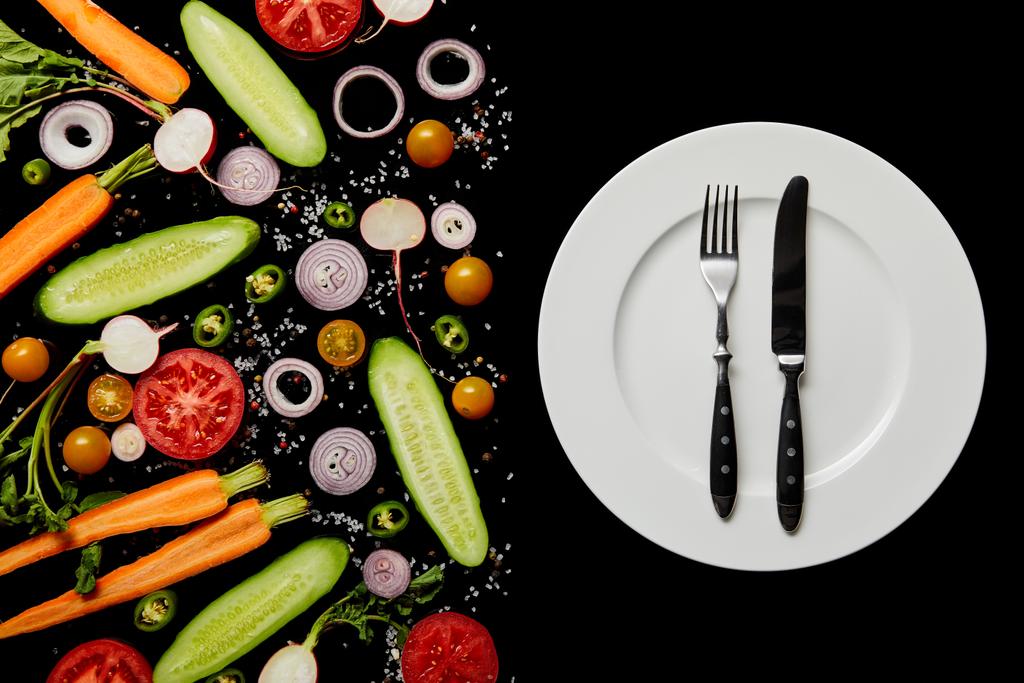 вид зверху круглої тарілки зі срібними столовими приборами біля овочевих скибочок ізольовані на чорному
 - Фото, зображення