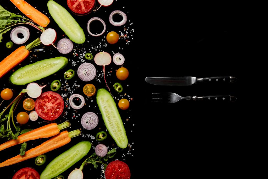 top view of fresh vegetable slices with salt near knife and fork isolated on black with copy space - Photo, Image