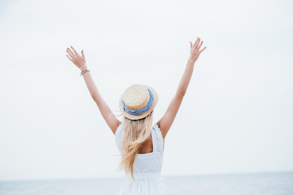 back view of young blonde woman in straw hat standing with outstretched hands  - Photo, Image