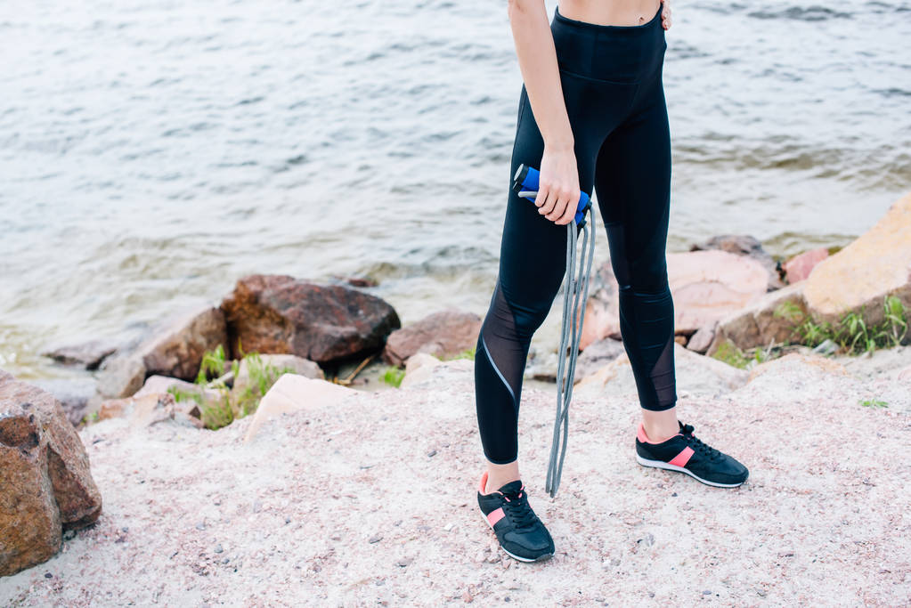 vista cortada de jovem esportista de pé perto do mar e segurando corda de salto
  - Foto, Imagem