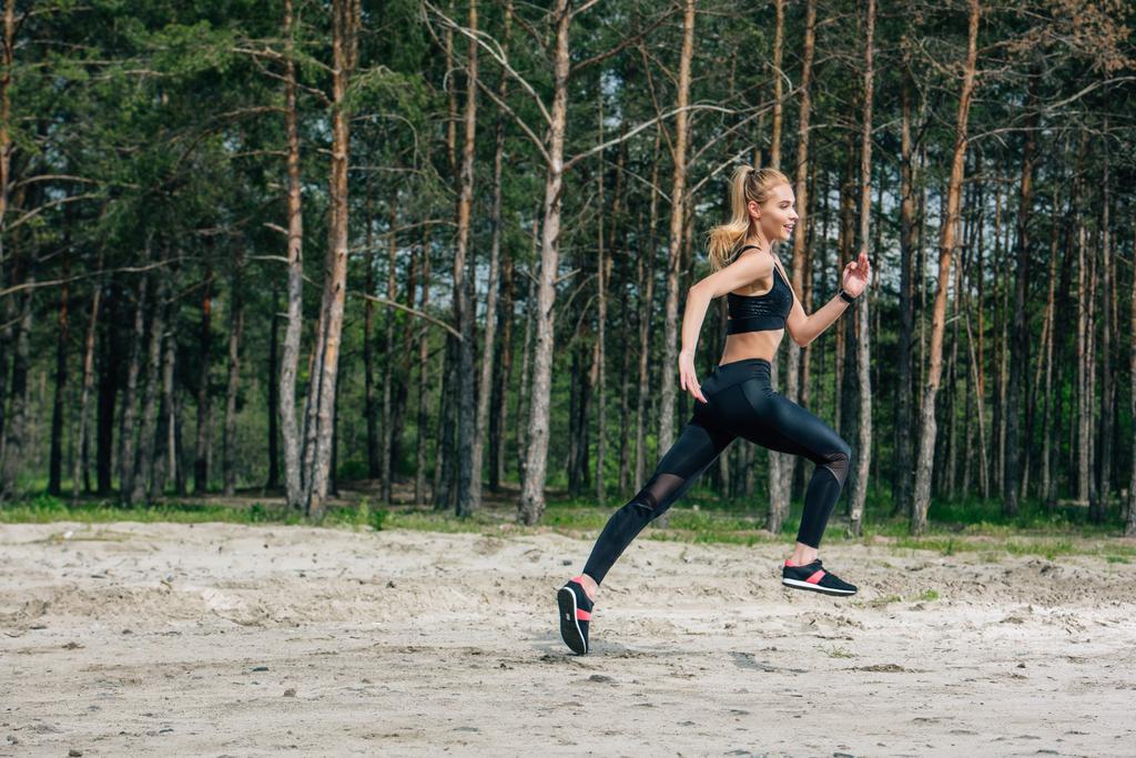 onnellinen ja urheilullinen blondi nainen juoksee lähellä vihreitä puita
  - Valokuva, kuva