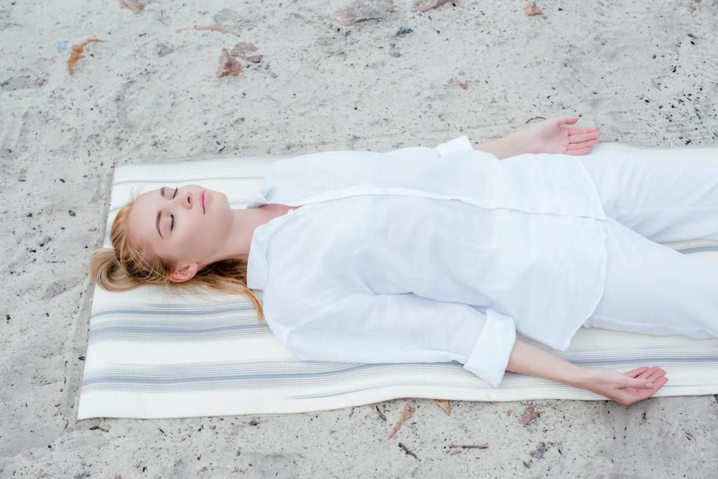 overhead view of attractive blonde woman with closed eyes meditating while lying on yoga mat - Photo, Image