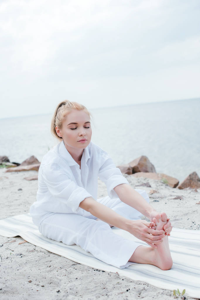 attraktive blonde Frau mit geschlossenen Augen dehnt sich auf Yogamatte  - Foto, Bild