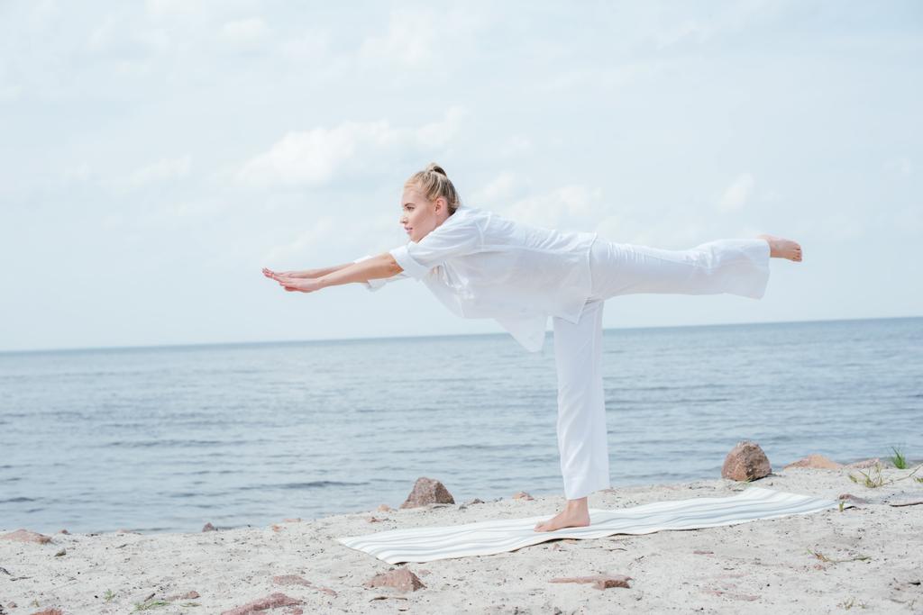 attractive blonde woman practicing yoga on yoga mat near sea  - Photo, Image