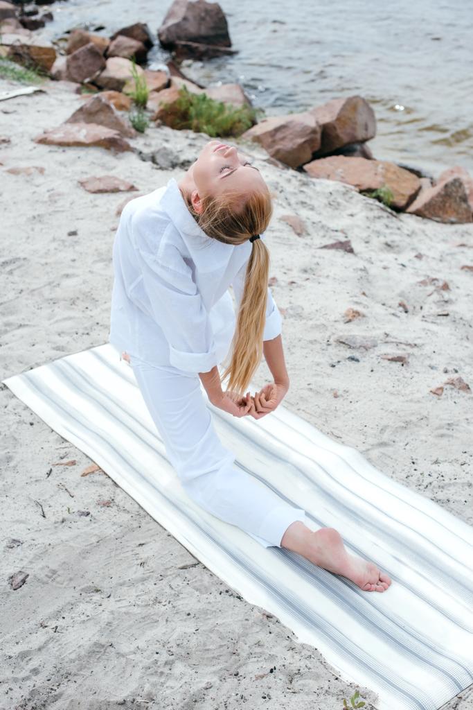 вид сверху привлекательной девушки с закрытыми глазами практикующей йогу на коврике для йоги возле моря
  - Фото, изображение