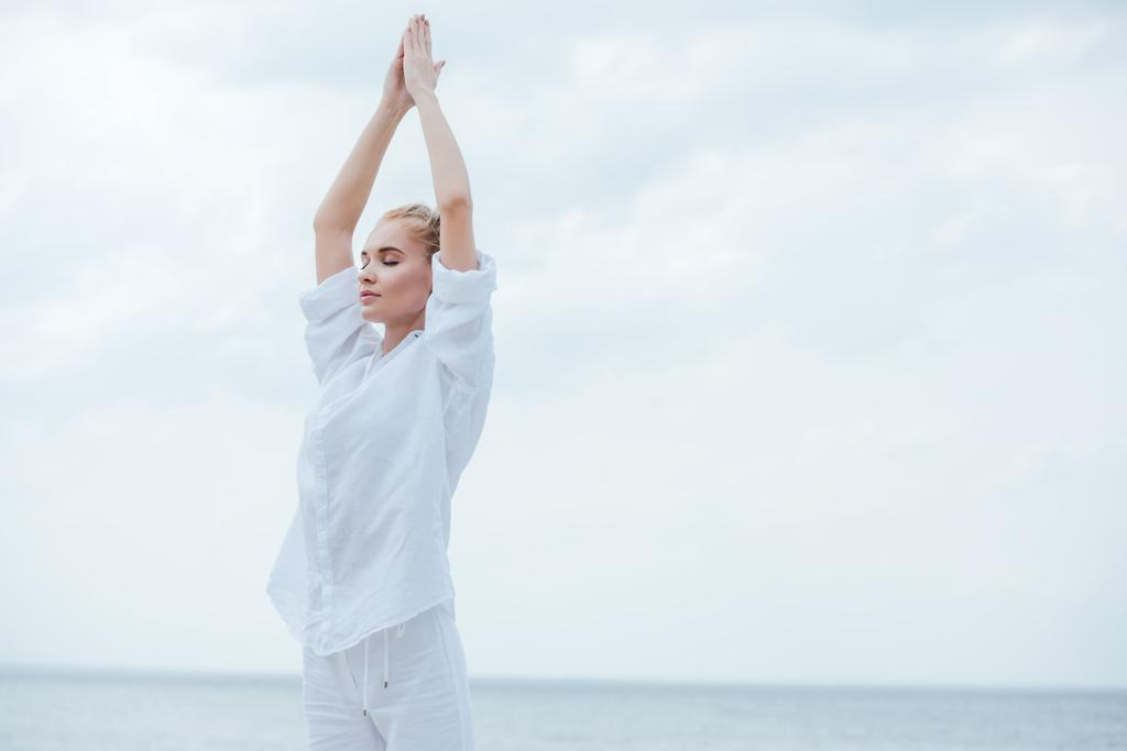 menina atraente com olhos fechados praticando ioga e de pé com as mãos de oração
  - Foto, Imagem